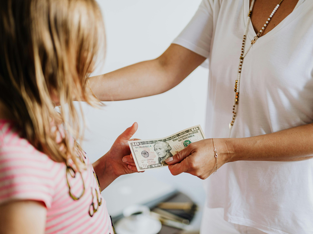 parent handing ten dollars to her daughter