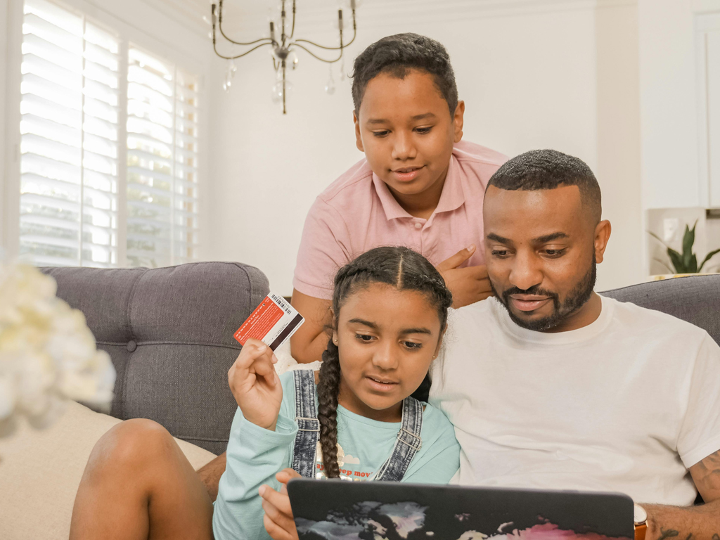 two children with their dad making a purchase on his laptop