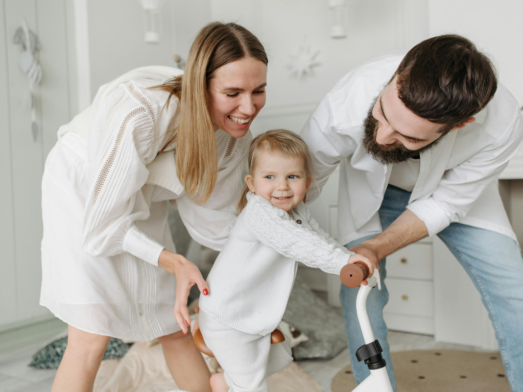 parents teaching their toddler how to use a tricycle