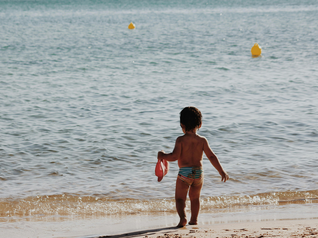 toddler standing on the sand looking out at the water