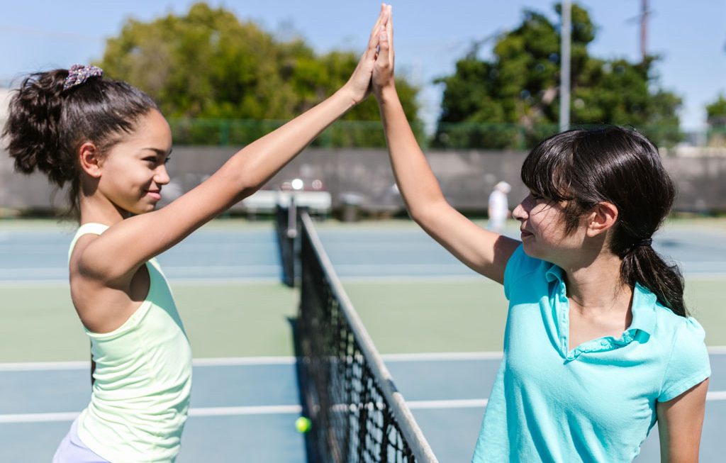 two girls giving a high five on the tennis court