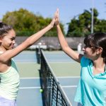 two girls giving a high five on the tennis court