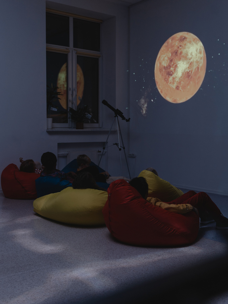 children on bean bag chairs looking at a moon projection