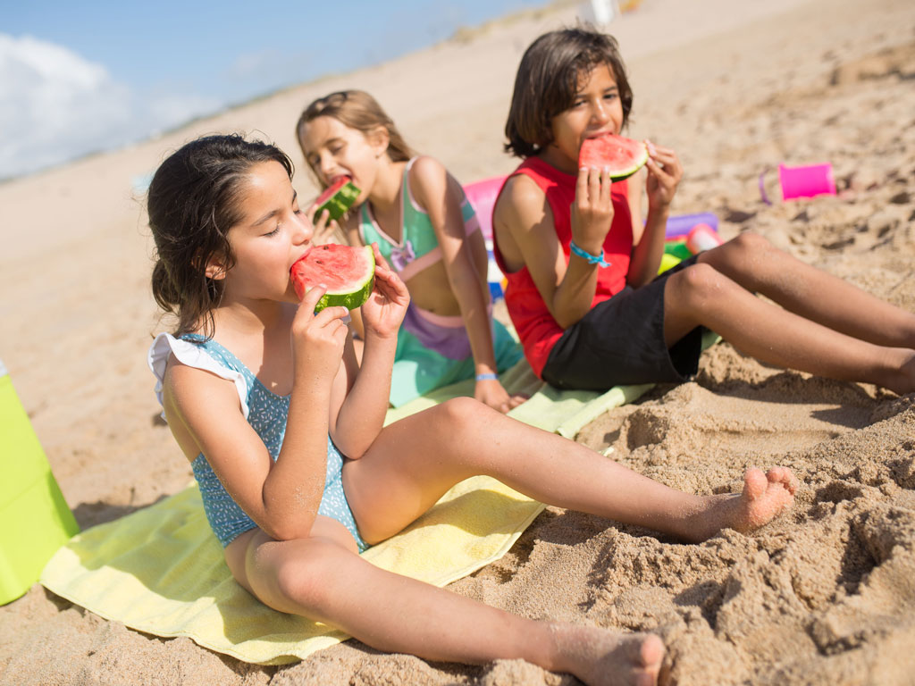 three kids eating watermelon at the beach