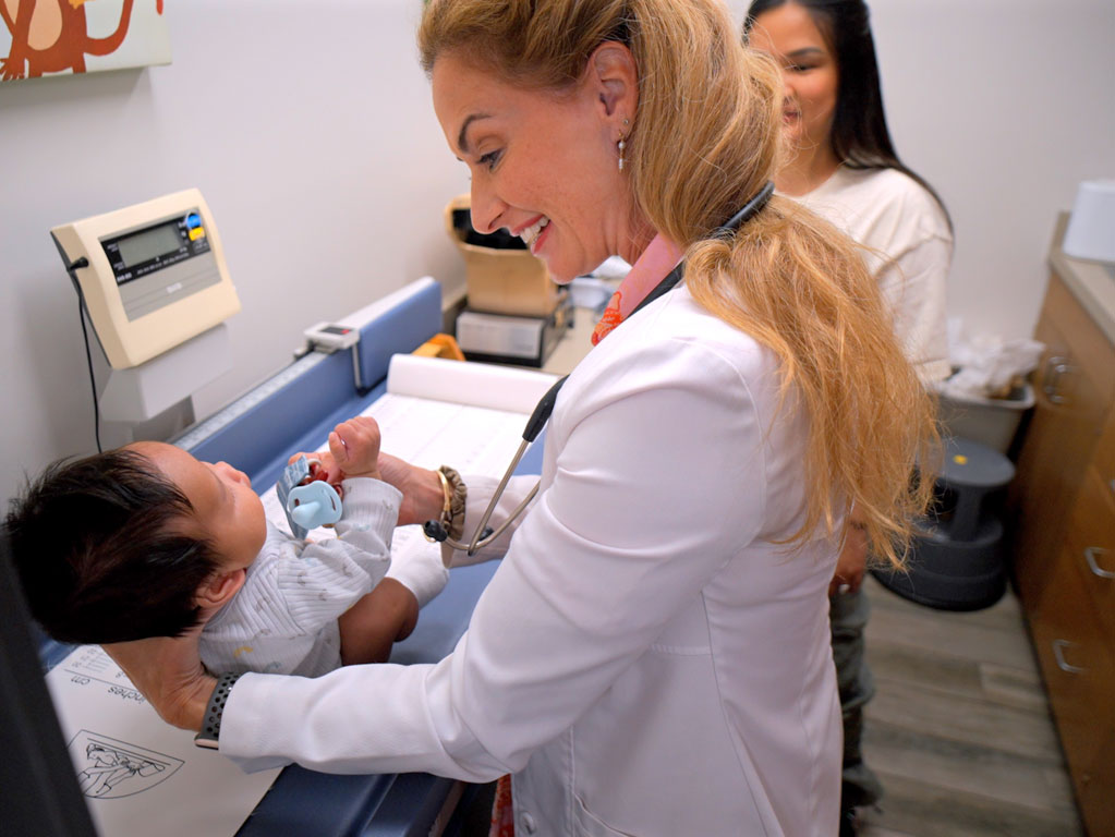 pediatrician holding infant while in the exam room with the infant's mom